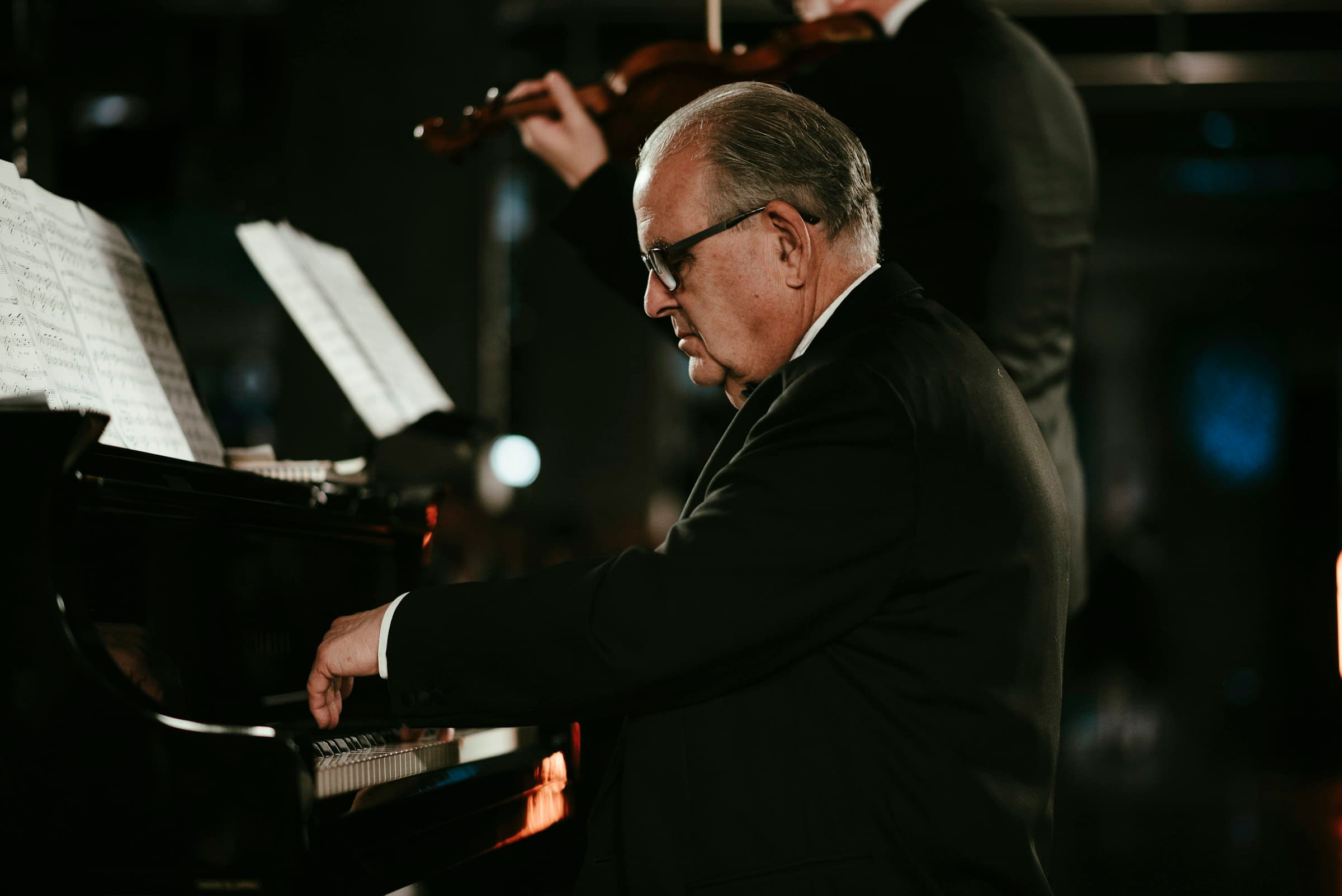 Pianist in a dark suit at the keys, a violinist behind him