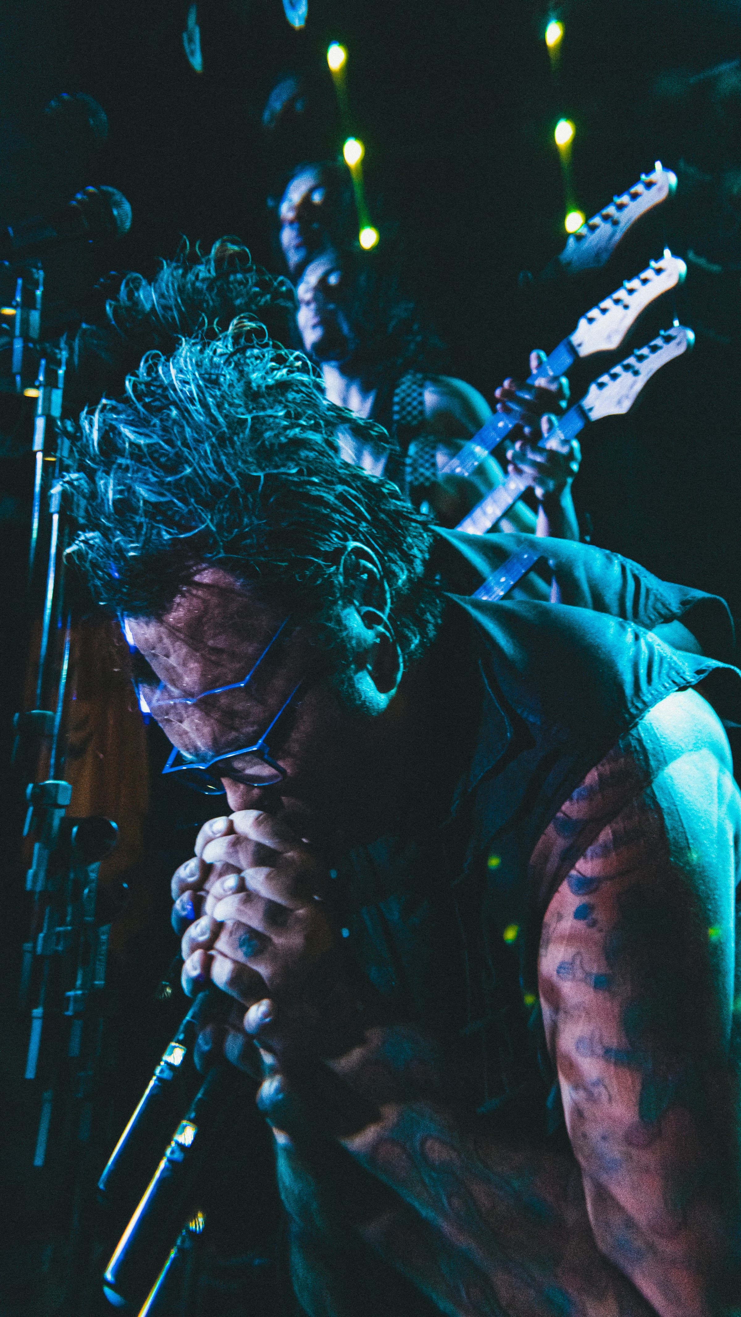 Singer with a guitar behind him, microphone at his mouth