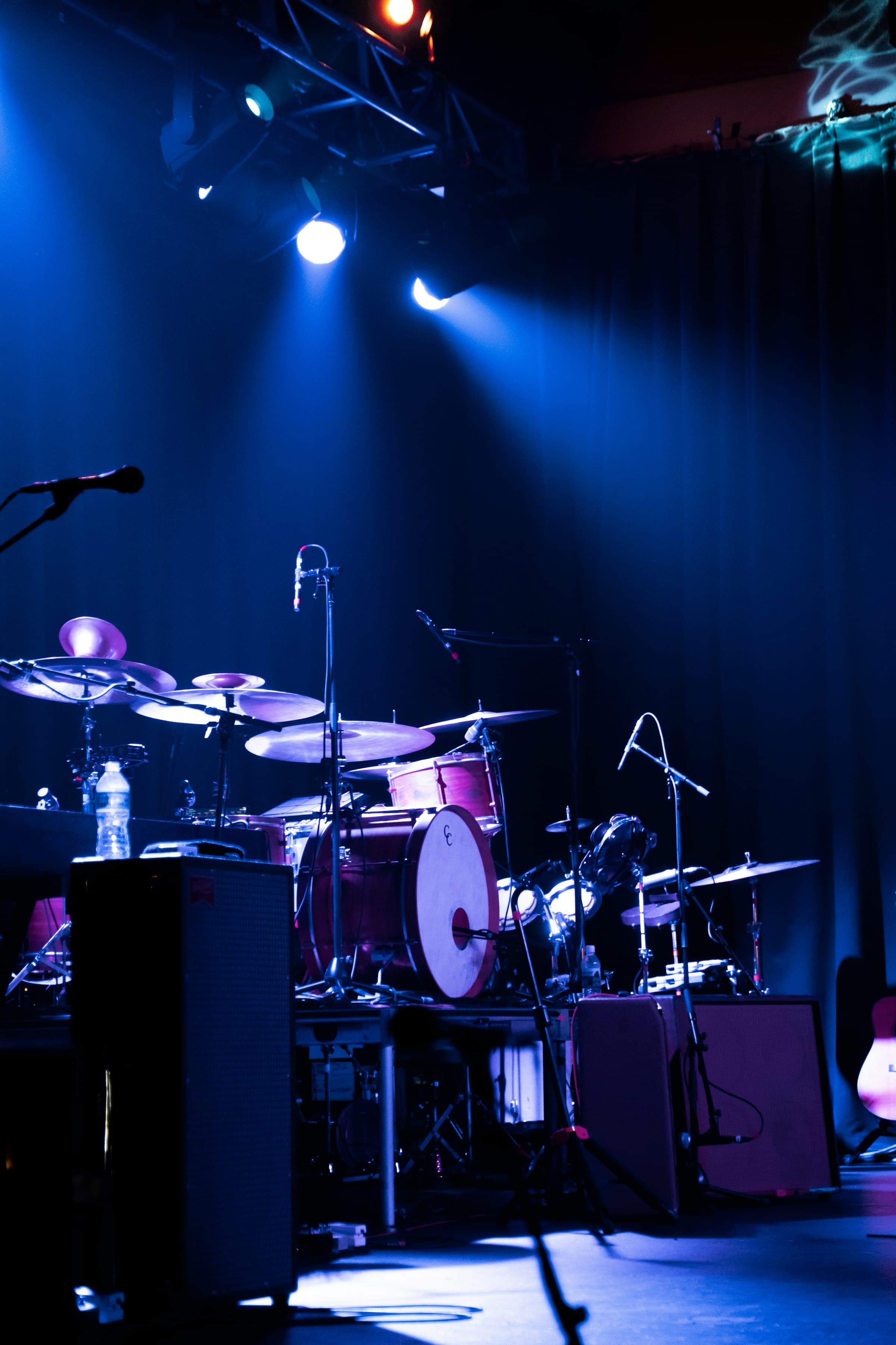 Drum kit and microphone stands on a stage under blue light