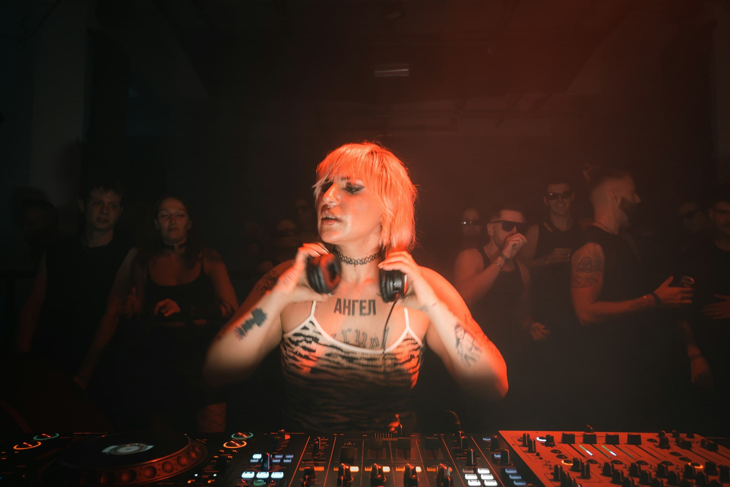 DJ in headphones at the decks, crowd behind her in red light